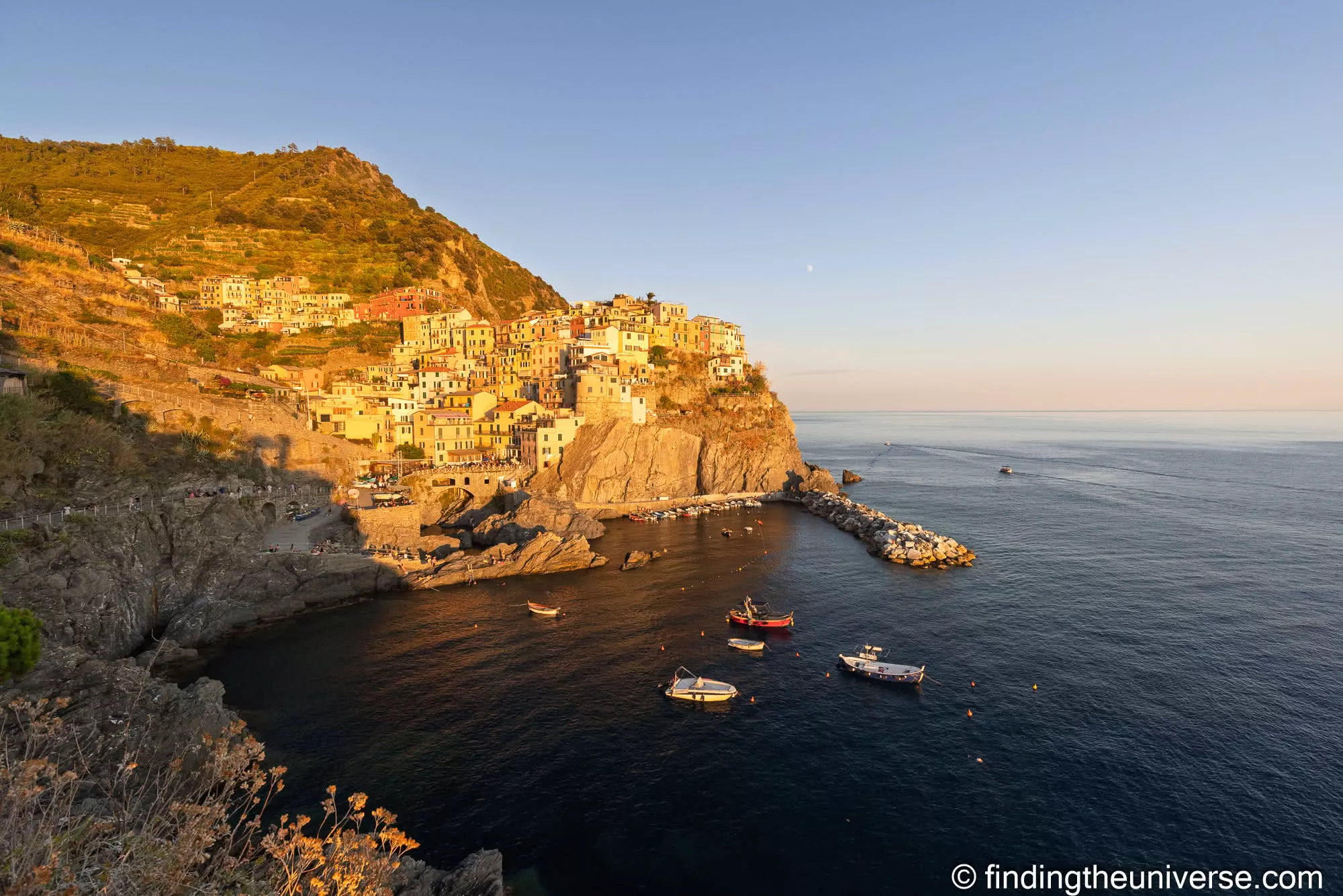 A sun-drenched coastal village at golden hour, terracotta rooftops spilling toward the sea